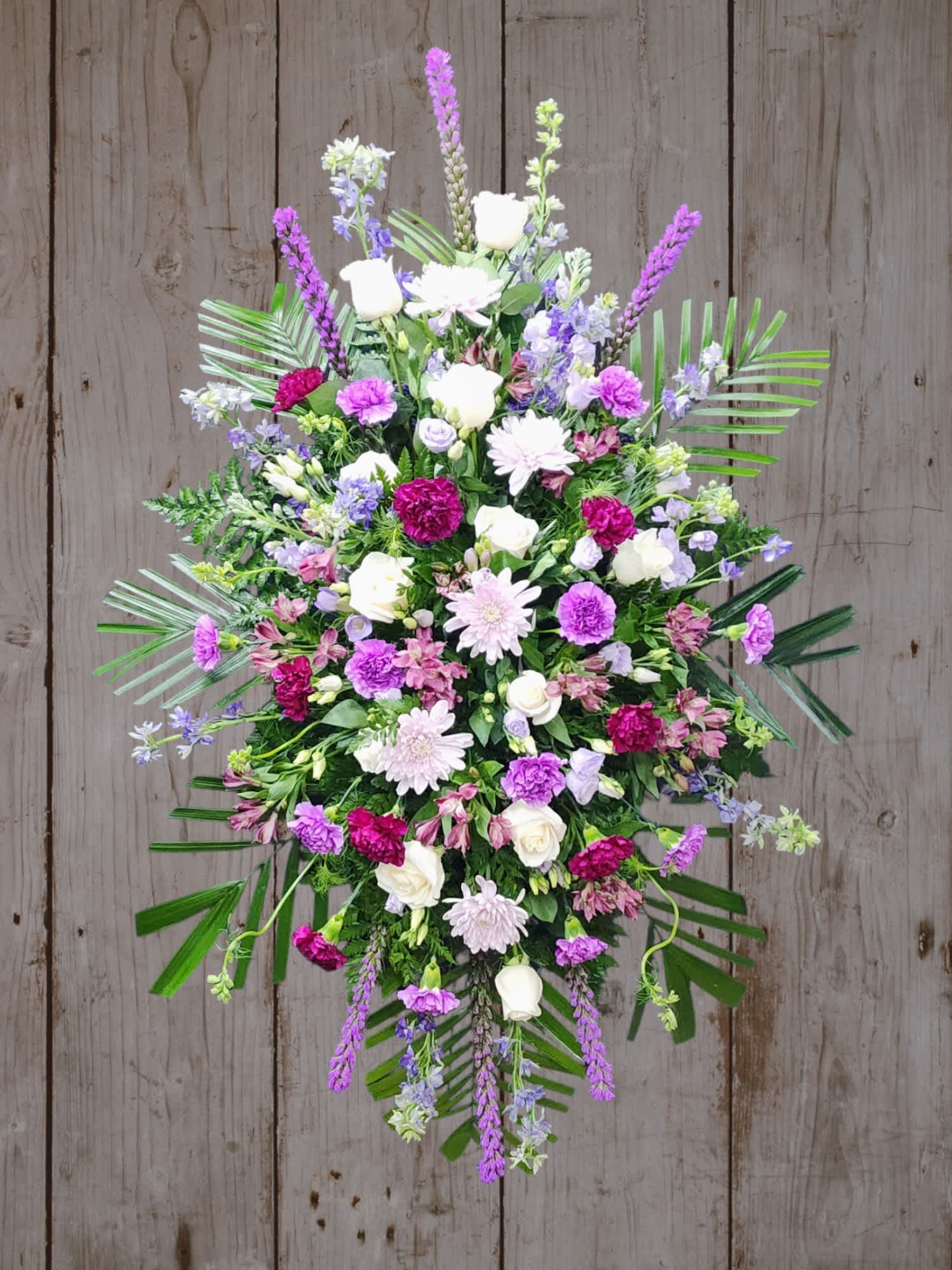 Lavender Reflections - Standing spray of creams, purples, and shades of lavender. Carnations, Roses and seasonal lavender flowers. A base of traditional greens including robalini, baker fern, and a touch of eucalyptus a generous display of love and a life well lived. 