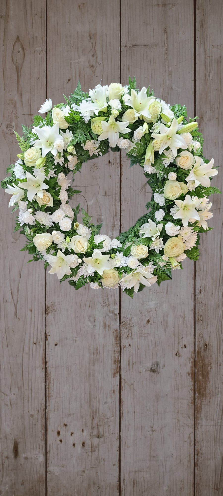 White floral wreath with lilies and roses on a wooden background