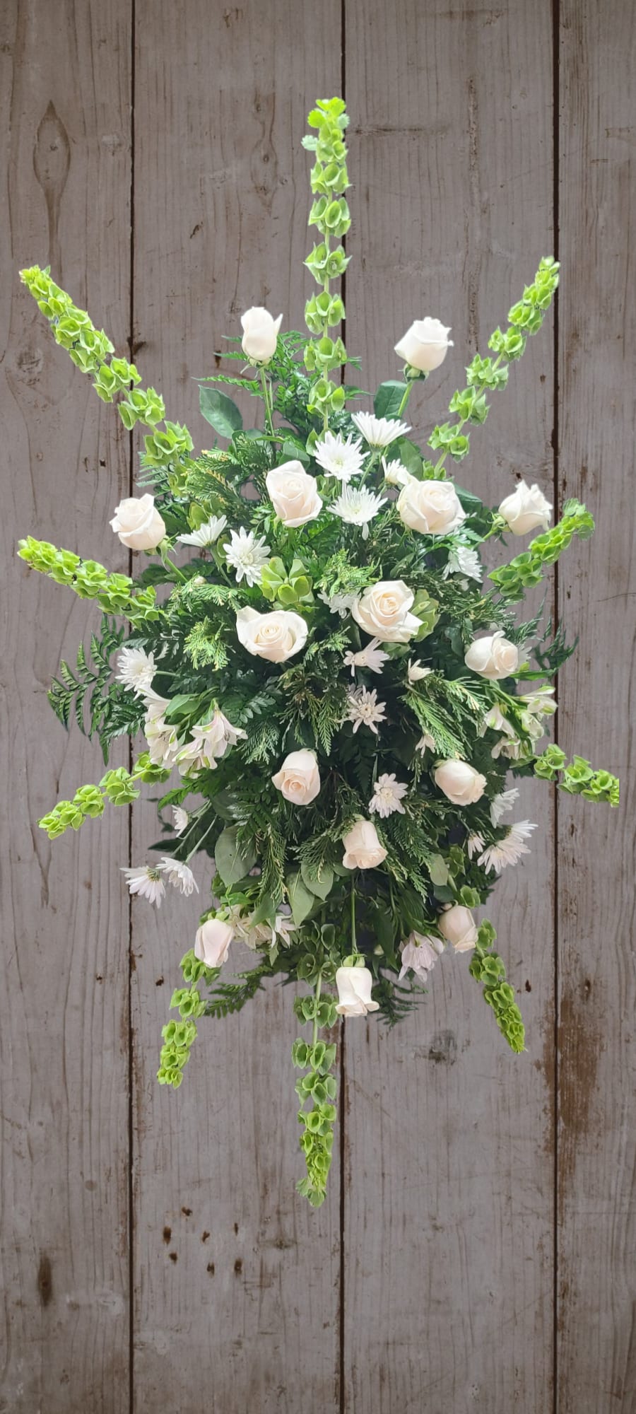 White roses and daisies arranged with green spikes in a starburst design