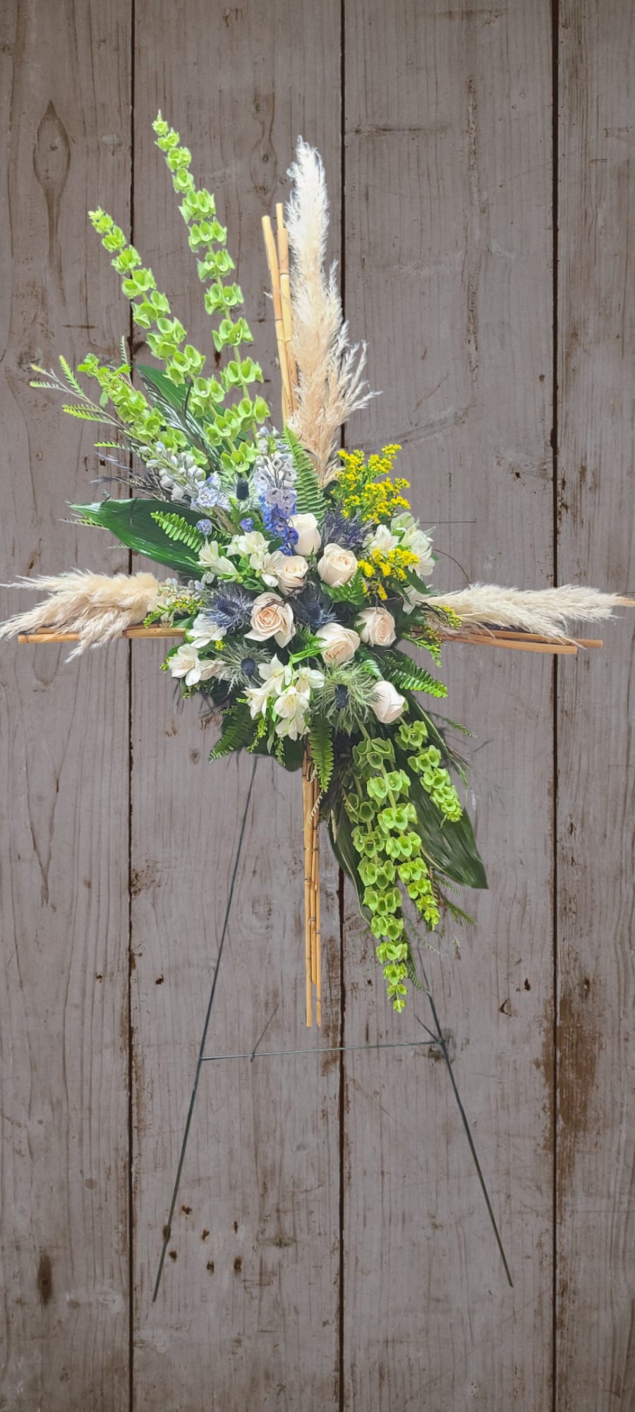 Floral cross arrangement with white roses, green orchids, and pampas grass