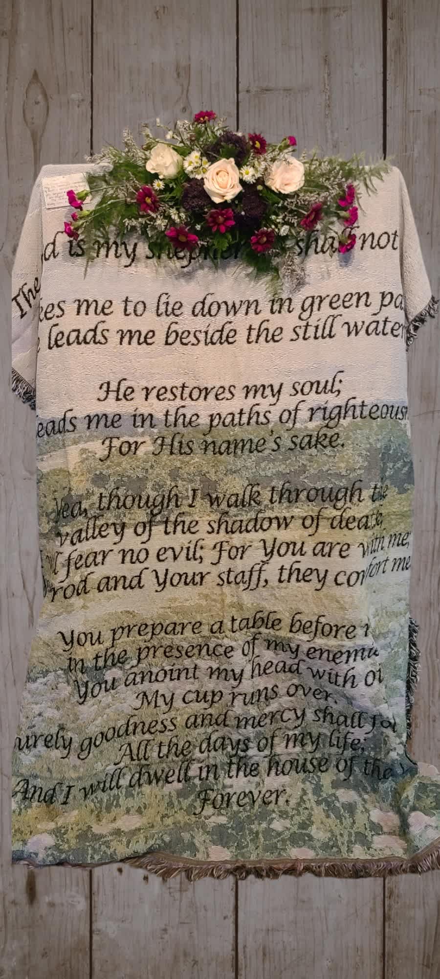 Floral arrangement on a Psalm-printed blanket hanging on a wooden wall
