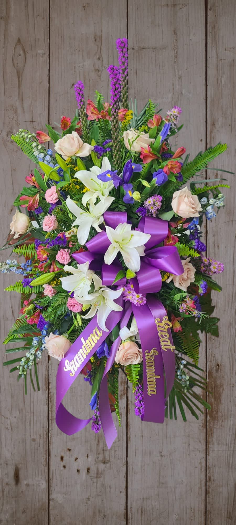 Standing floral spray with white lilies, pale roses, and a purple ribbon bow
