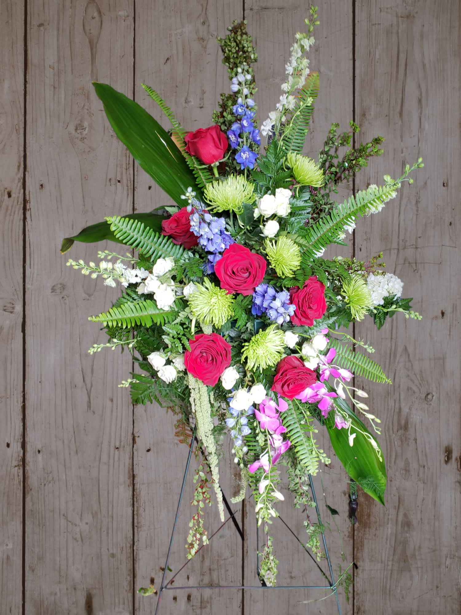 Touch of the Tropics - Tropical touches of orchids add to this bright, modern standing spray. Mixed greenery, roses, and fugi mums add elegance and texture. 