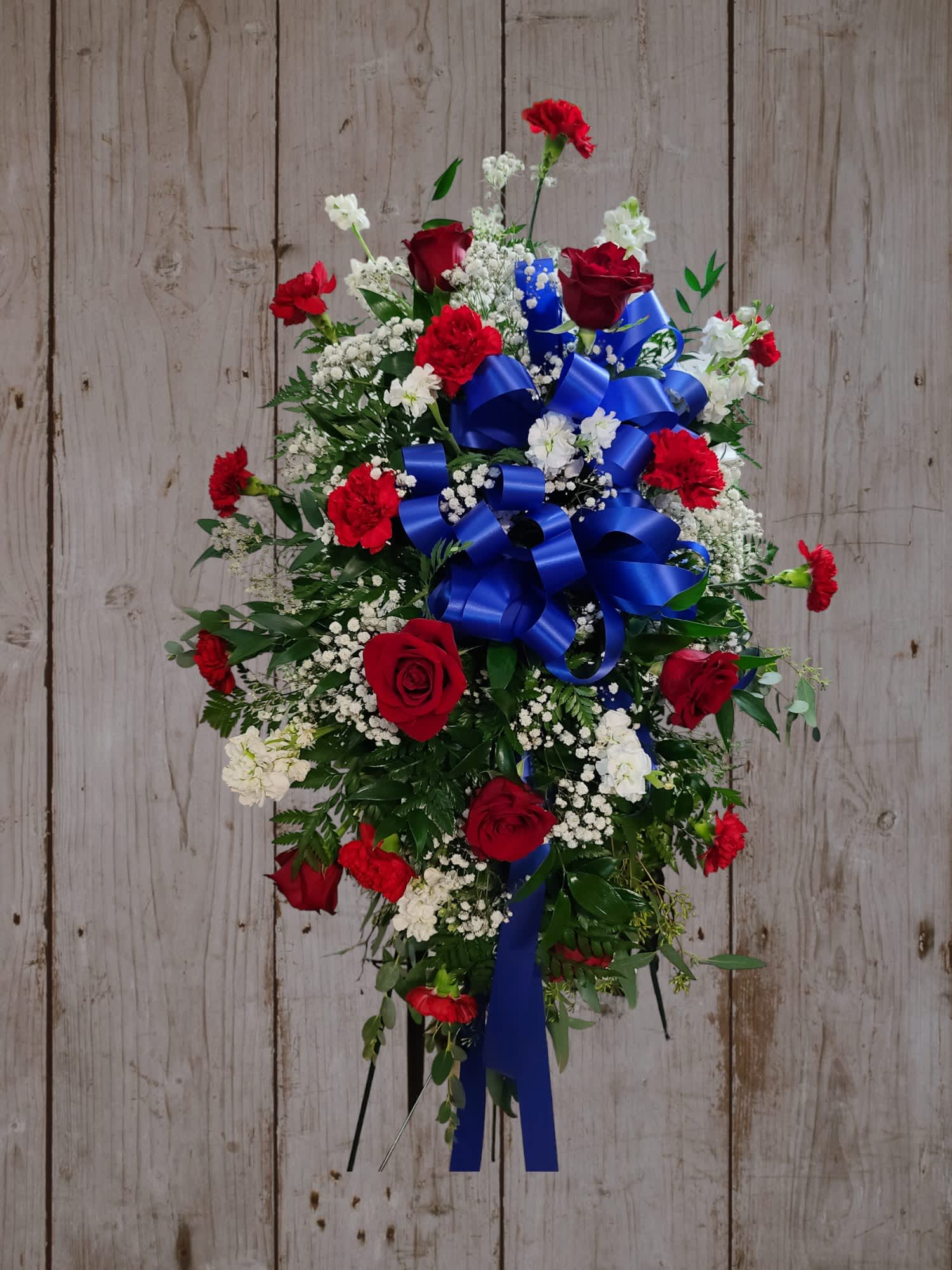 Standing floral spray with red roses, carnations, and blue ribbon