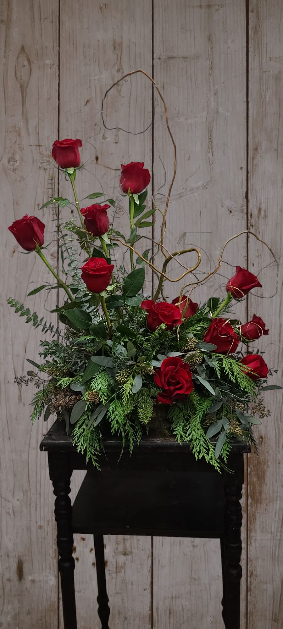 Red roses arranged in a low black container with curly branches