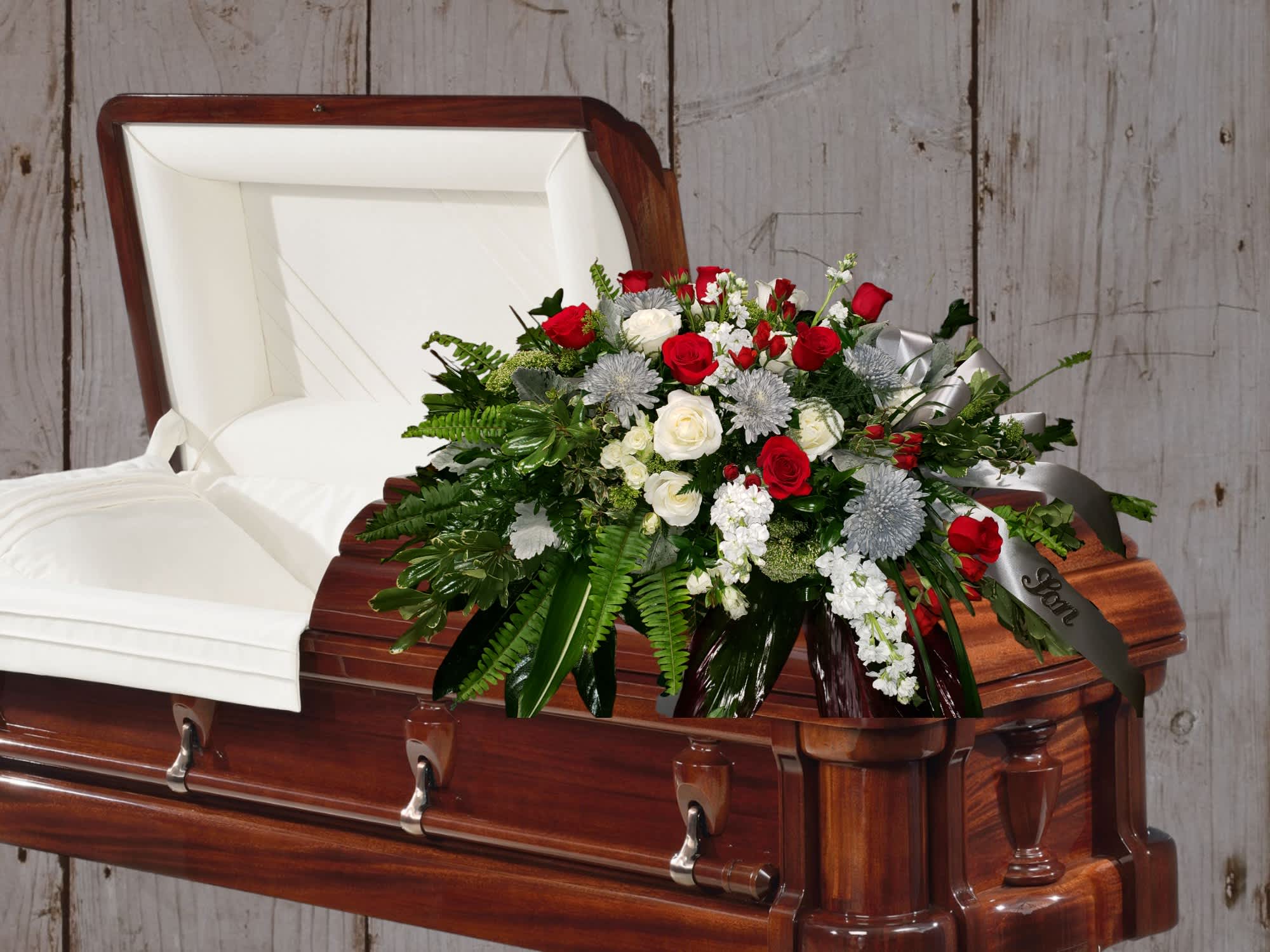 Casket spray of red and white roses with greenery on a wooden casket