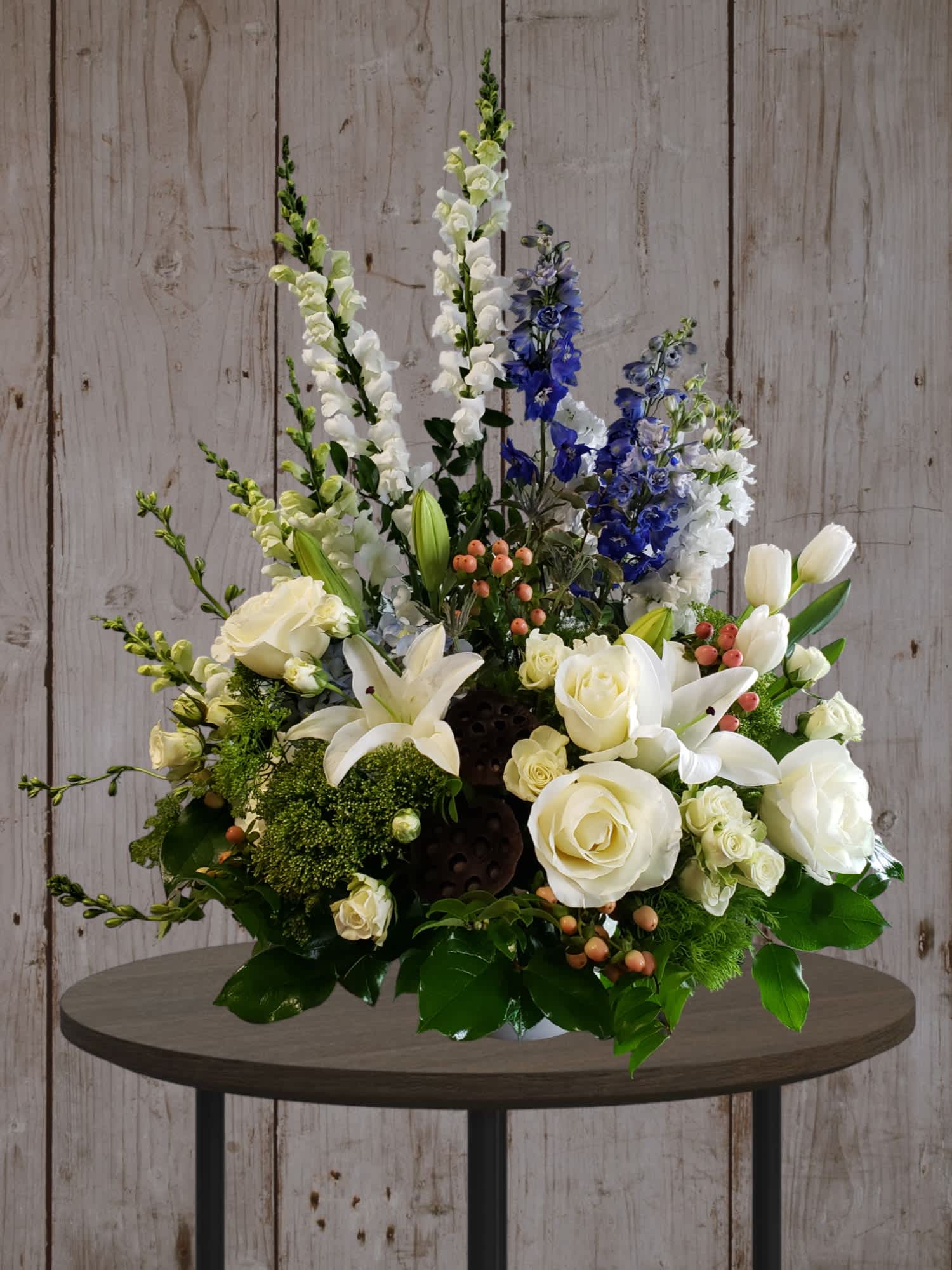 White roses and lilies with blue delphinium in a low arrangement