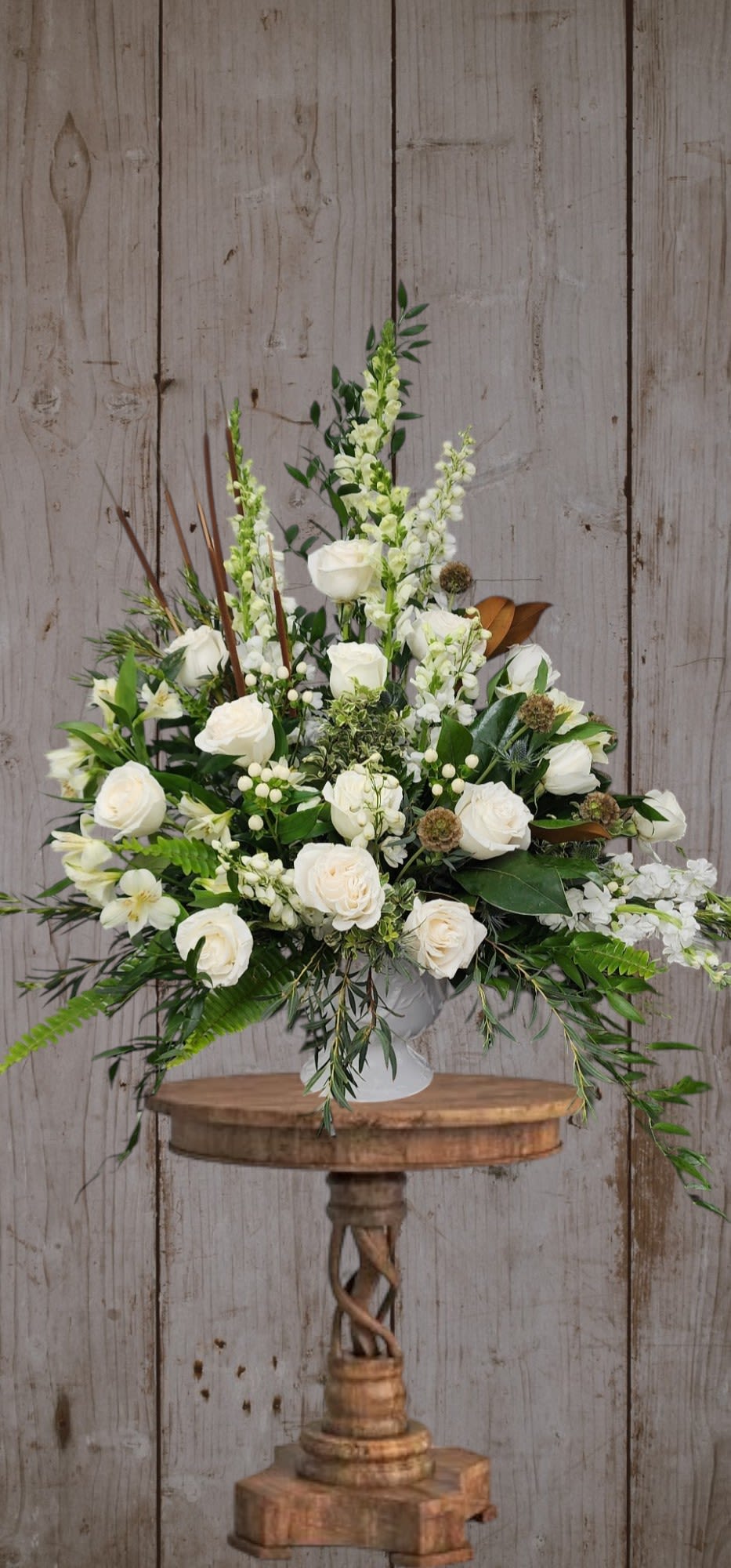 White rose arrangement in a white vase with mixed greenery