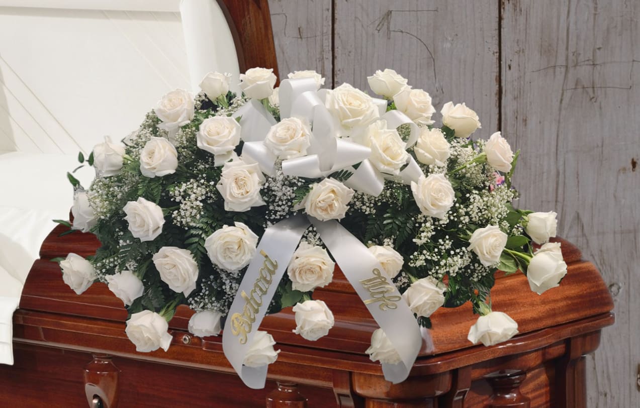 White rose casket spray with satin ribbon on a wooden casket