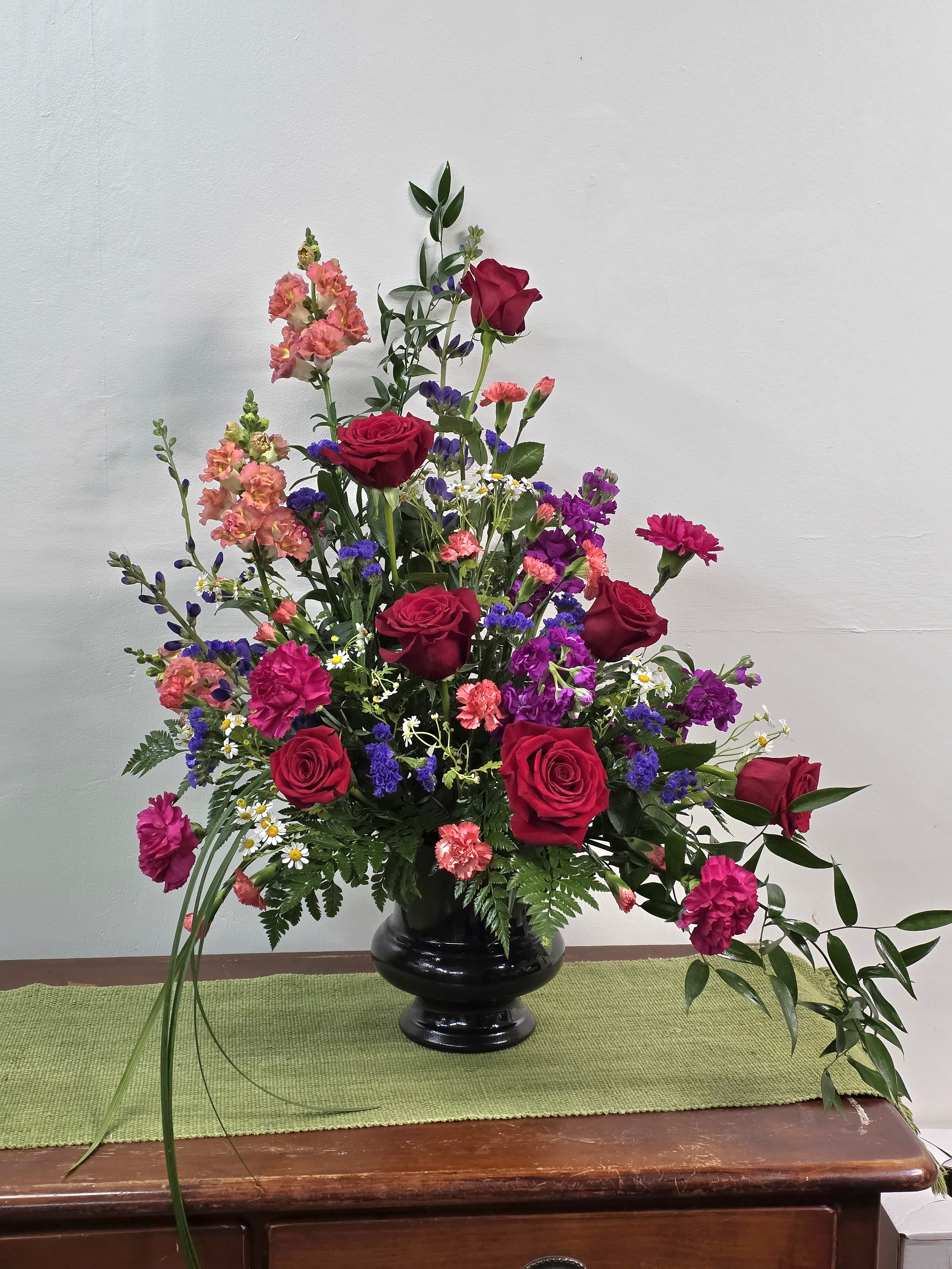 Hot to Trott - This spicy arrangement is made for the Bold. Lush red roses, hot pink carnations, Orange spray carnations, snap dragons, and Purple statice create a bold expression of love, friendship, and a well lived life. 