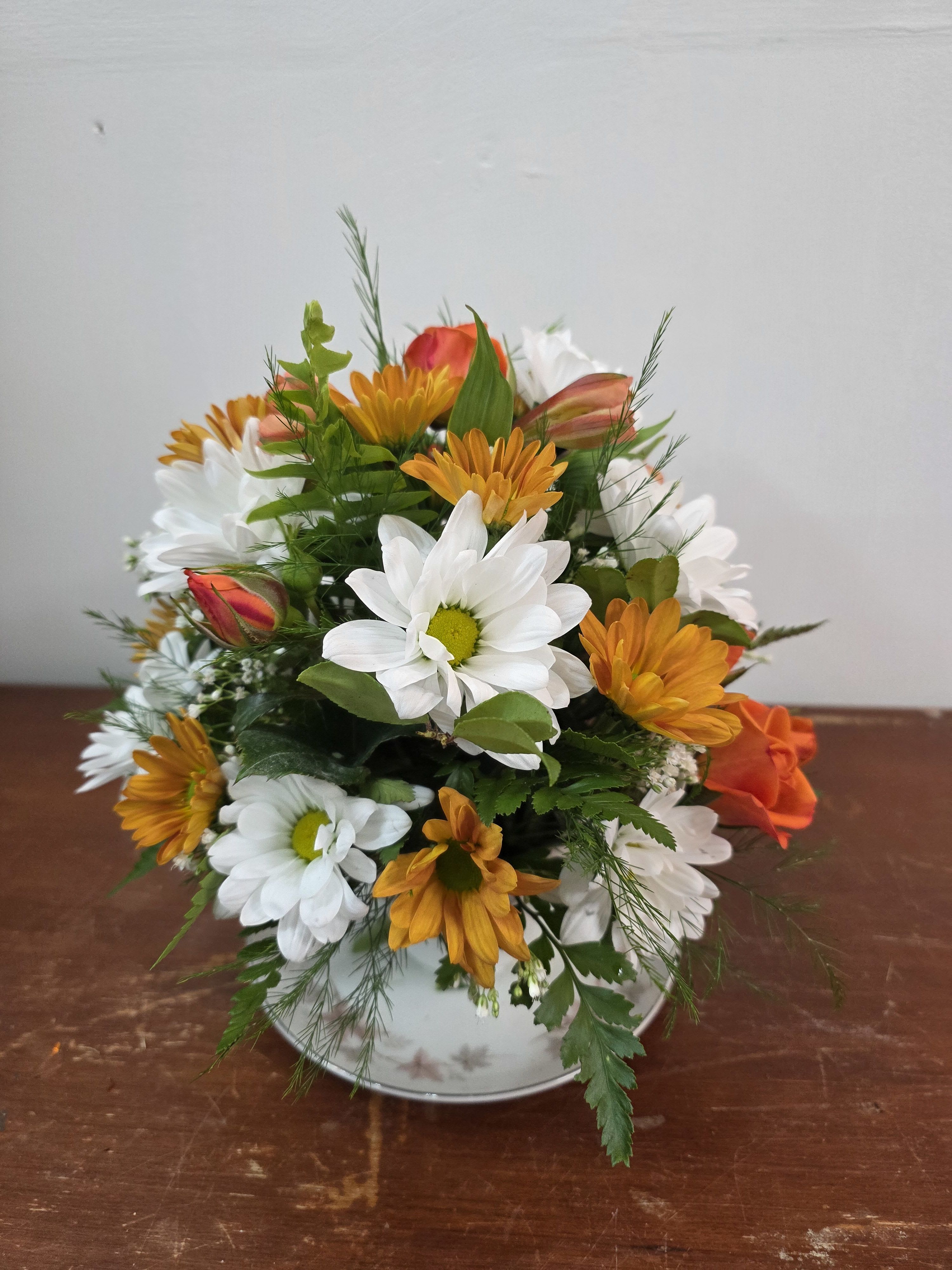 Mixed bouquet of white and orange daisies in a white vase
