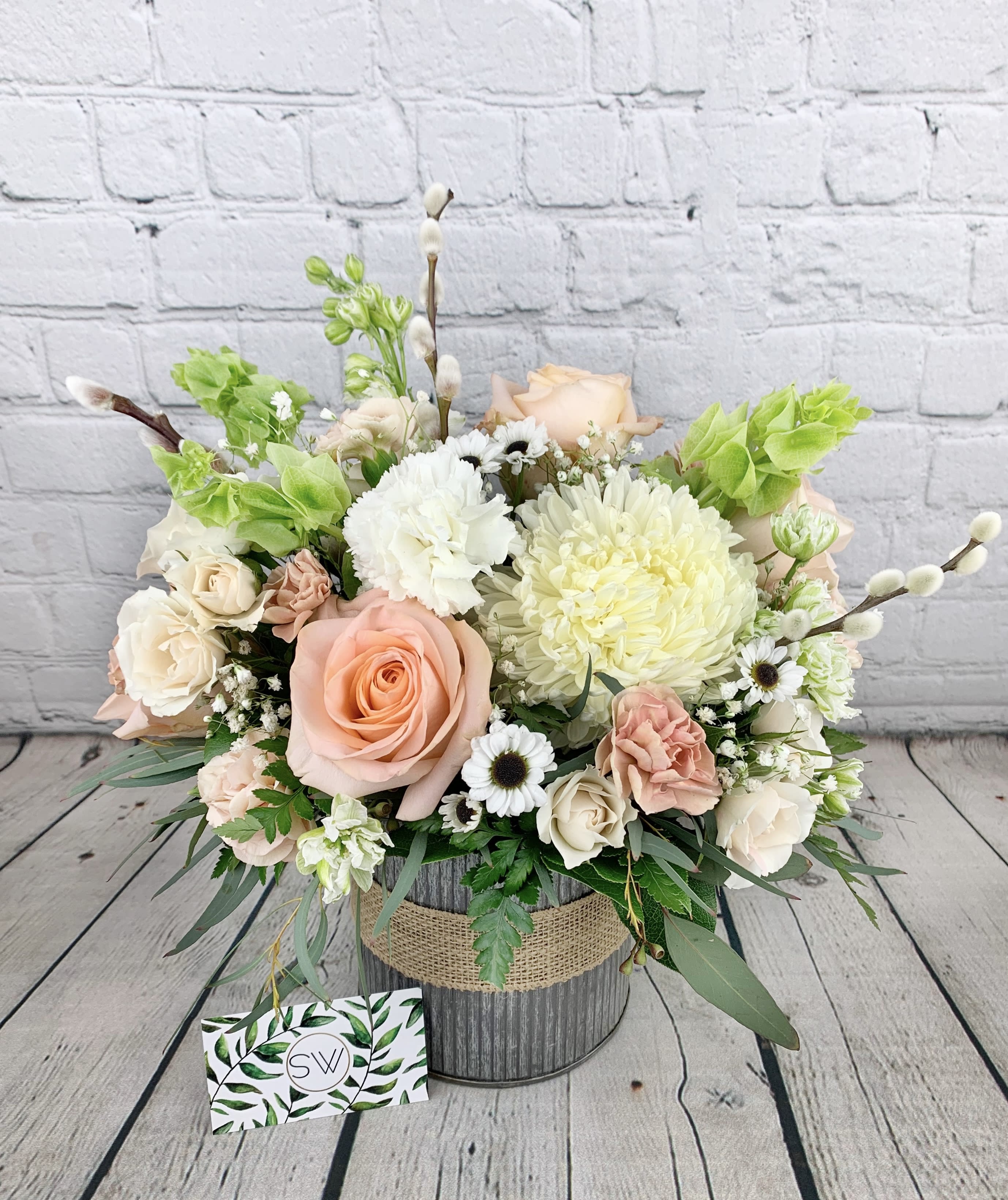 Pastel flower arrangement with roses, chrysanthemums, and daisies in a rustic container
