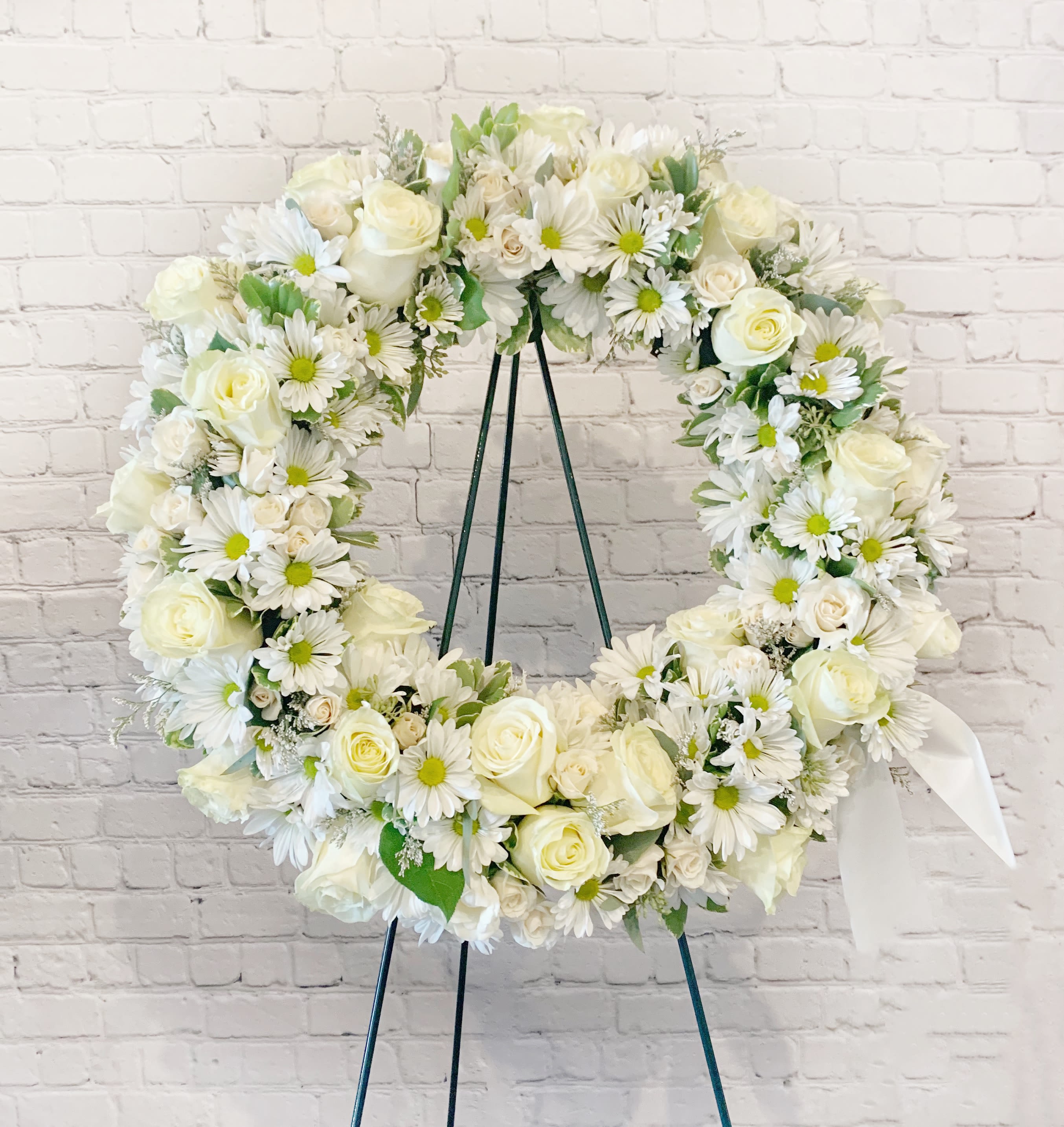 White floral wreath on a stand with roses and daisies