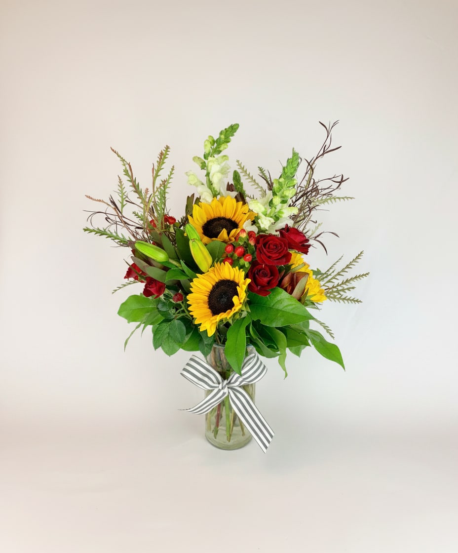 Sunflowers and red roses in a glass vase with a striped ribbon
