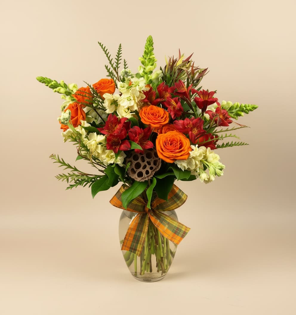 Orange roses and red alstroemeria in a glass vase with a plaid ribbon