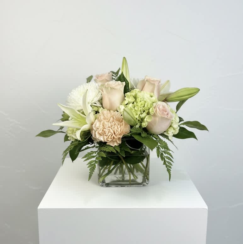 Cream roses and white lilies arranged in a clear glass vase