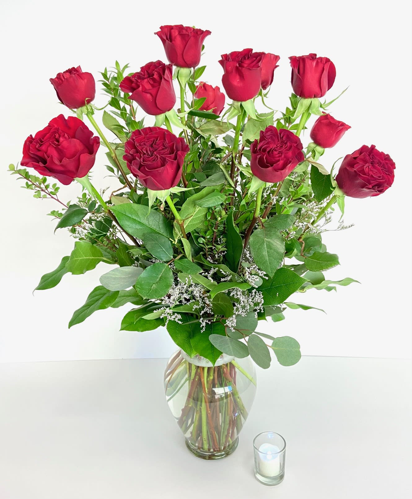 Red roses arranged in a clear glass vase with greenery