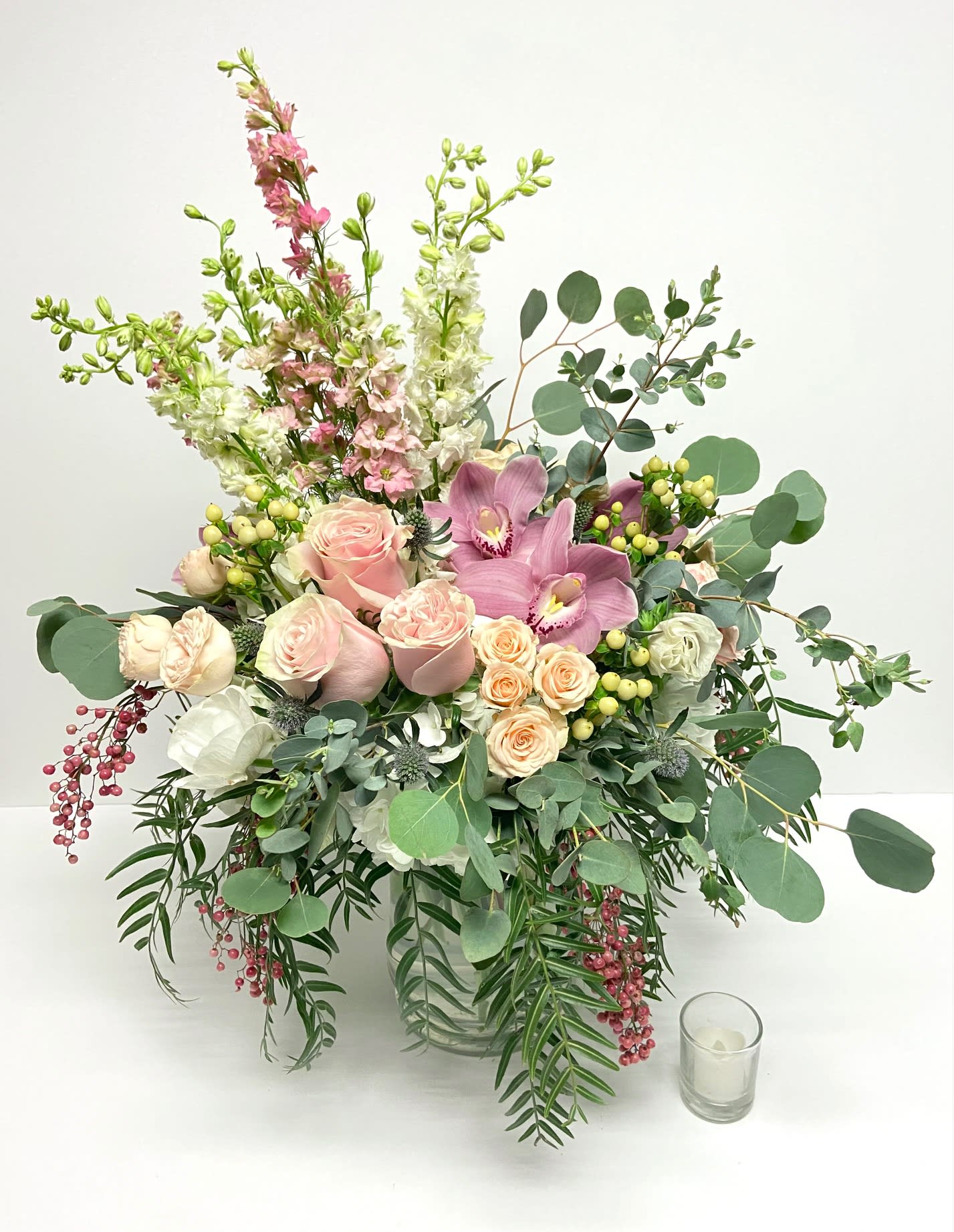 Large pastel bouquet in a clear glass vase with pink roses and orchids