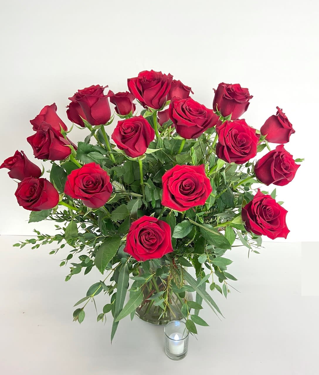 Bouquet of red roses in a clear glass vase with a small candle nearby
