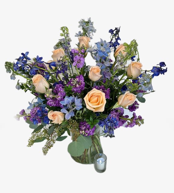 Peach roses and blue-purple flowers in a glass vase with a candle