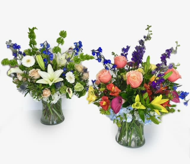 Two mixed flower arrangements in glass vases, one white and blue and one pink, yellow, and purple.