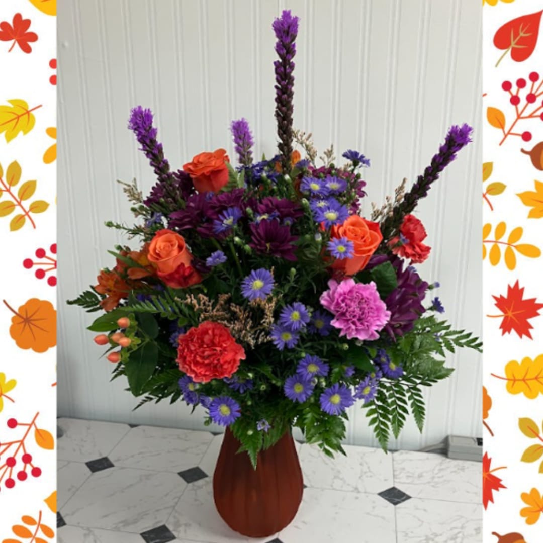Colorful mixed flower arrangement in a tall vase with purple spikes and orange roses