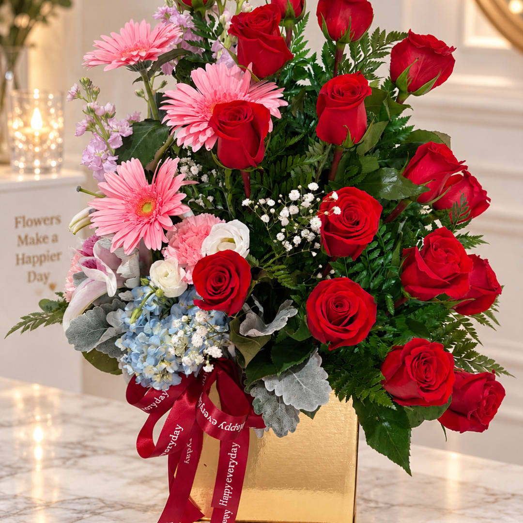 Bouquet of red roses and pink daisies in a gold box with a red ribbon