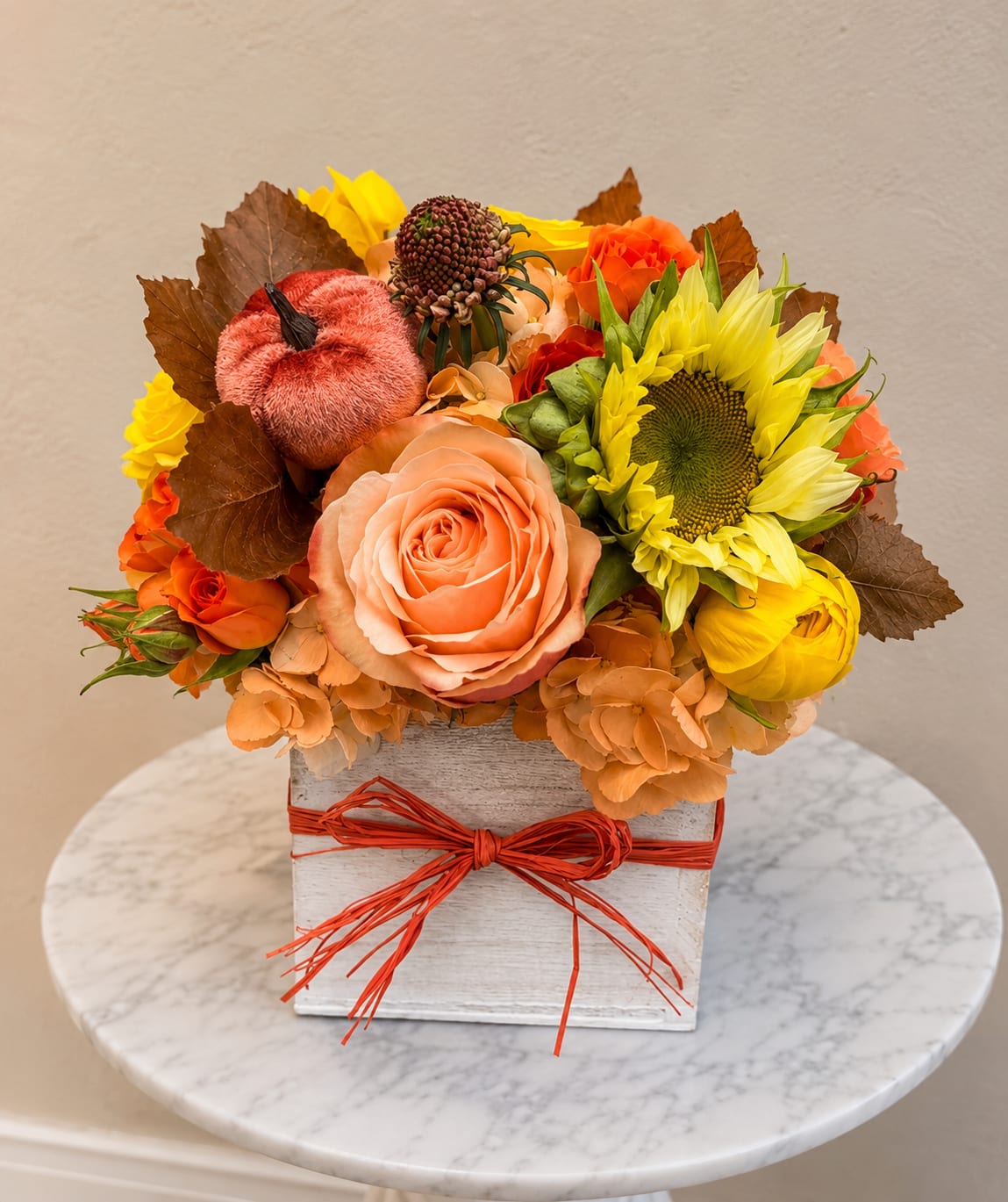 Autumn floral arrangement with roses and a sunflower in a square box