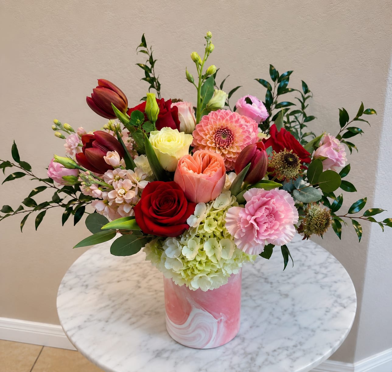 Mixed bouquet of roses, tulips, dahlias, and carnations in a pink vase