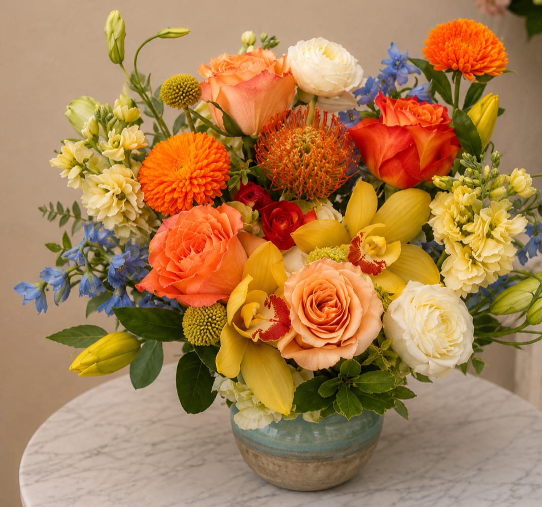 Mixed bouquet of orange, yellow, white, and blue flowers in a ceramic vase