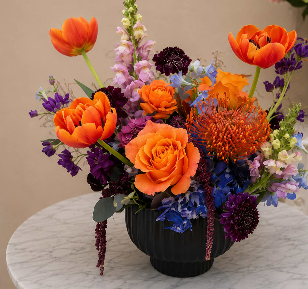 Bright mixed bouquet in a black vase with orange, purple, and blue flowers