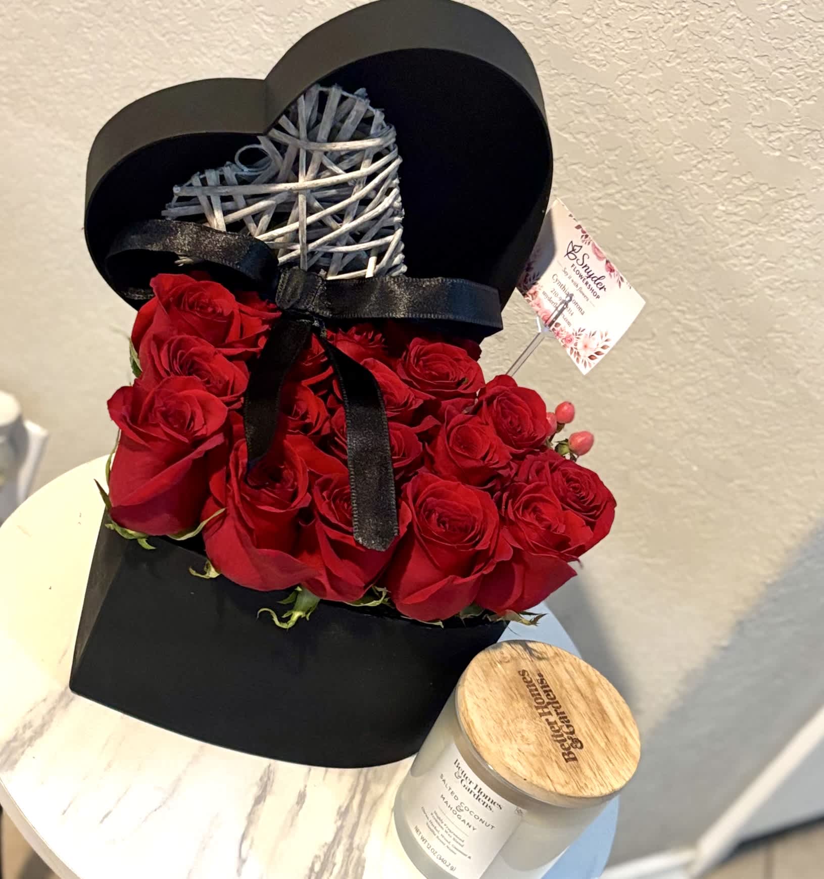Red roses arranged in a black heart-shaped box with a ribbon and wicker heart topper