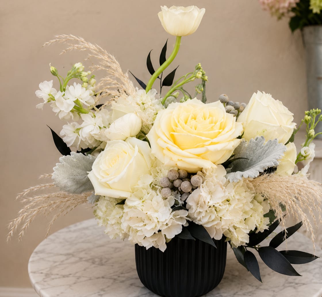 Cream roses and white flowers in a black vase with dried grasses