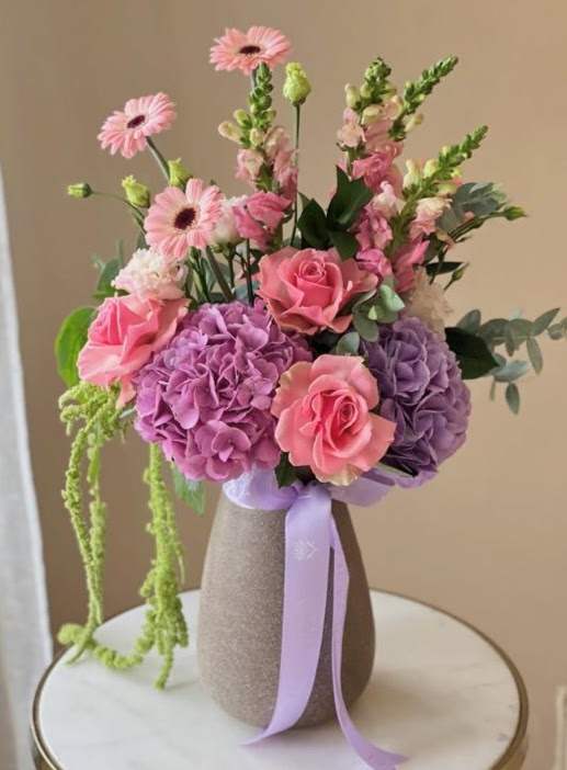 Pink and purple bouquet in a textured vase with a lavender ribbon