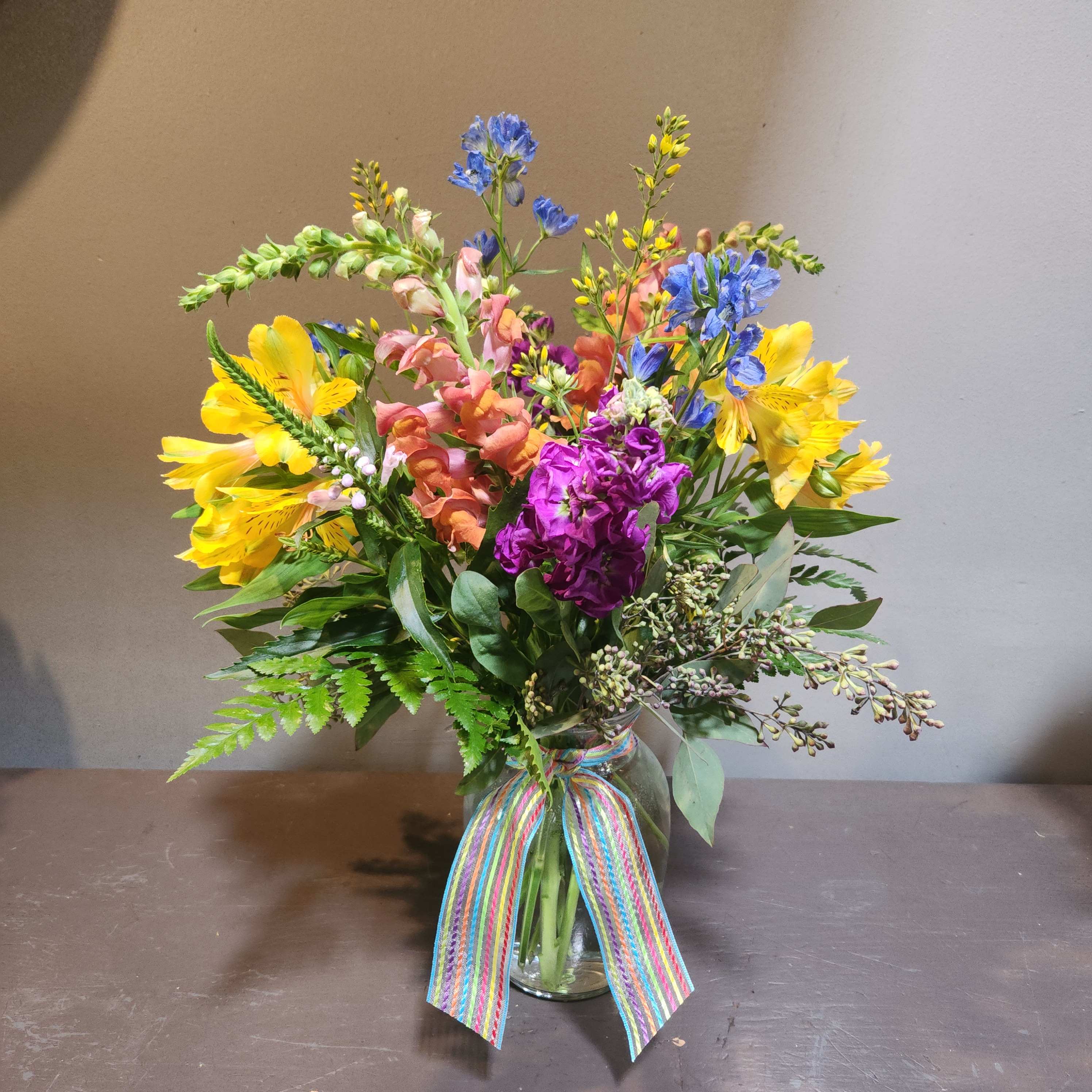 Colorful mixed bouquet in a glass vase with a rainbow ribbon