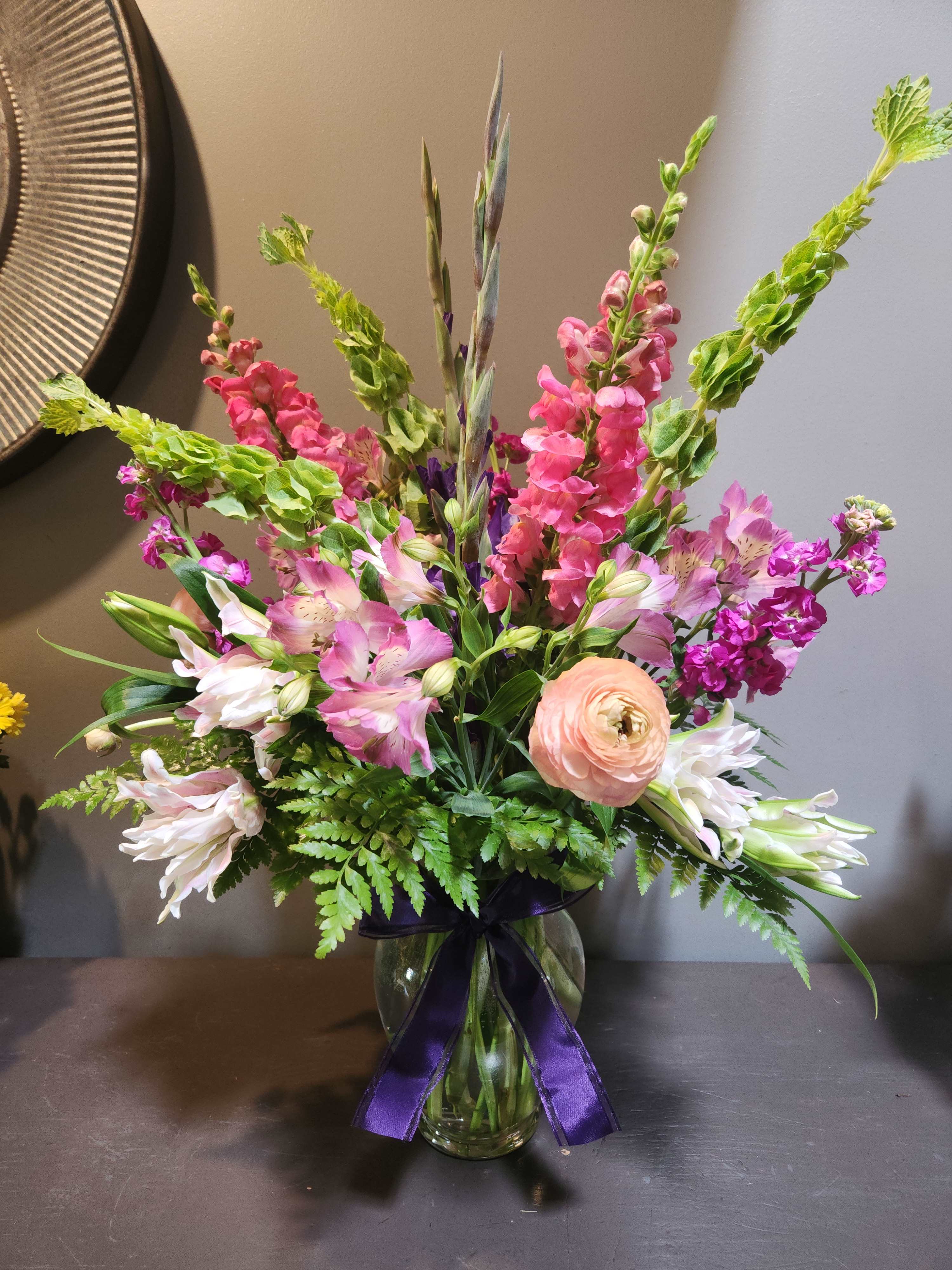Mixed pink and white flowers in a glass vase with a purple ribbon