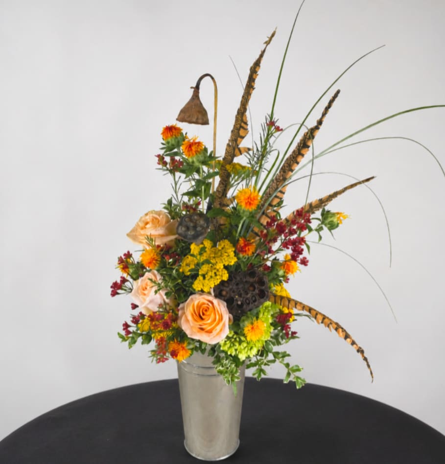 Tall mixed flower arrangement in a clear vase with peach roses and orange blooms