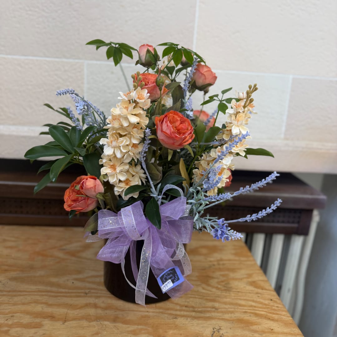 Mixed bouquet of peach roses and pale flowers in a dark vase with a purple ribbon