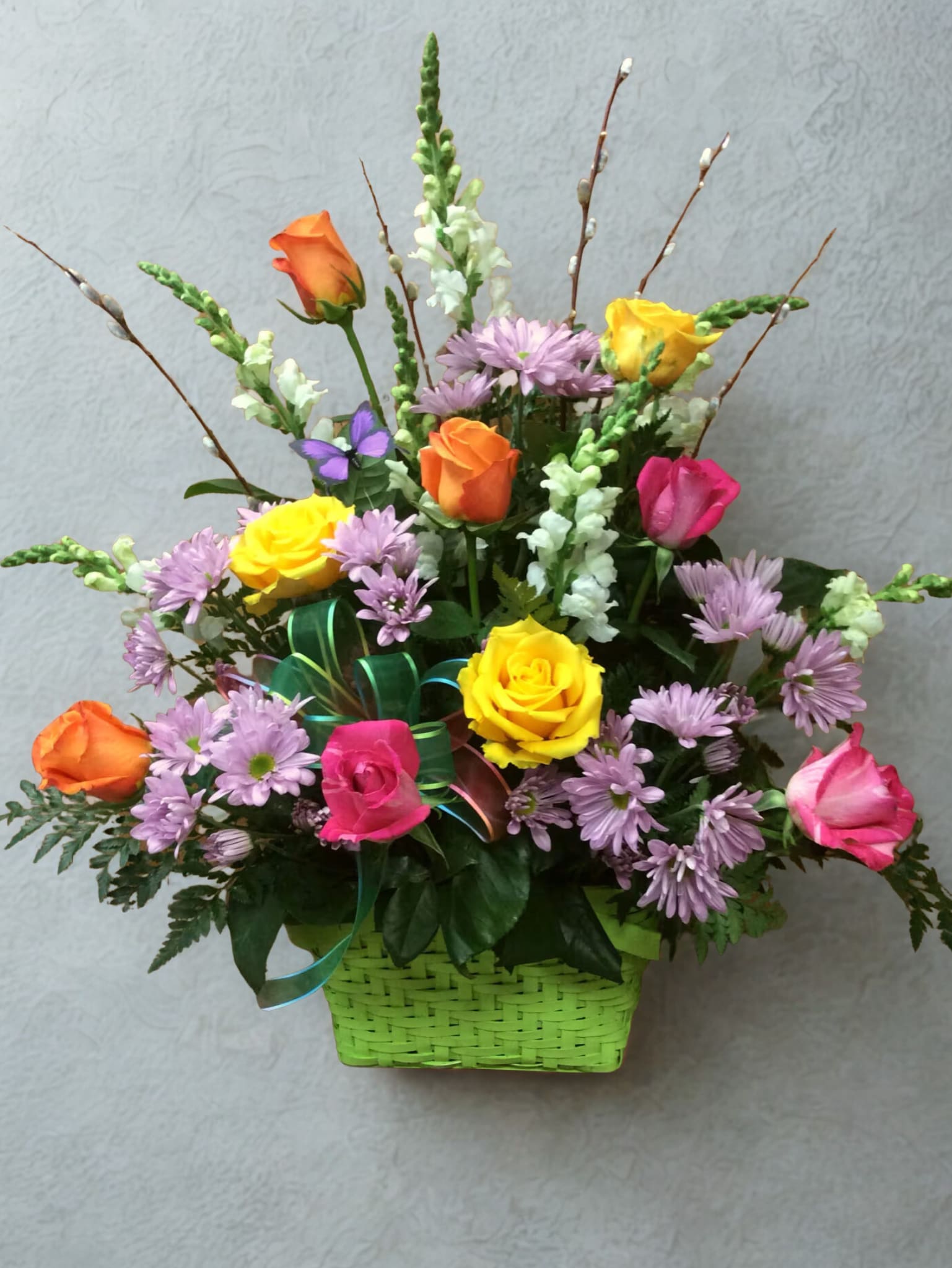 Mixed bouquet of roses and purple daisies in a green basket