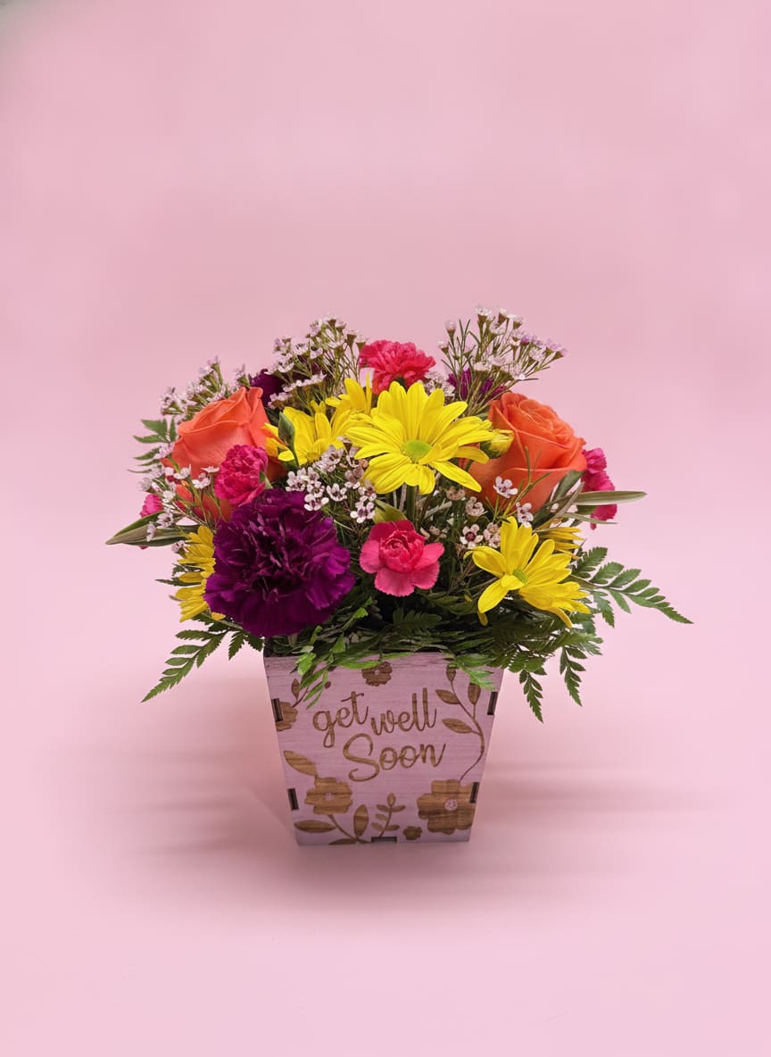 Bright Days Ahead - Bright Days Ahead is a cheerful, uplifting arrangement designed in a rustic wooden container etched with “Get Well,” offering a heartfelt message of comfort and care. Sunny yellow daisies bring a fresh burst of optimism, while orange roses add warmth and encouragement. Hot pink mini carnations and soft purple carnations create a lively, comforting contrast, and delicate pink waxflower weaves through for a gentle, airy finish.  Full of color, energy, and positivity, this design is made to brighten hospital rooms, recovery spaces, or any moment that calls for a little extra encouragement. The engraved wooden container serves as a lasting keepsake reminder that brighter days are always ahead.   All flowers, floral colors, and containers are subject to change due to availability.