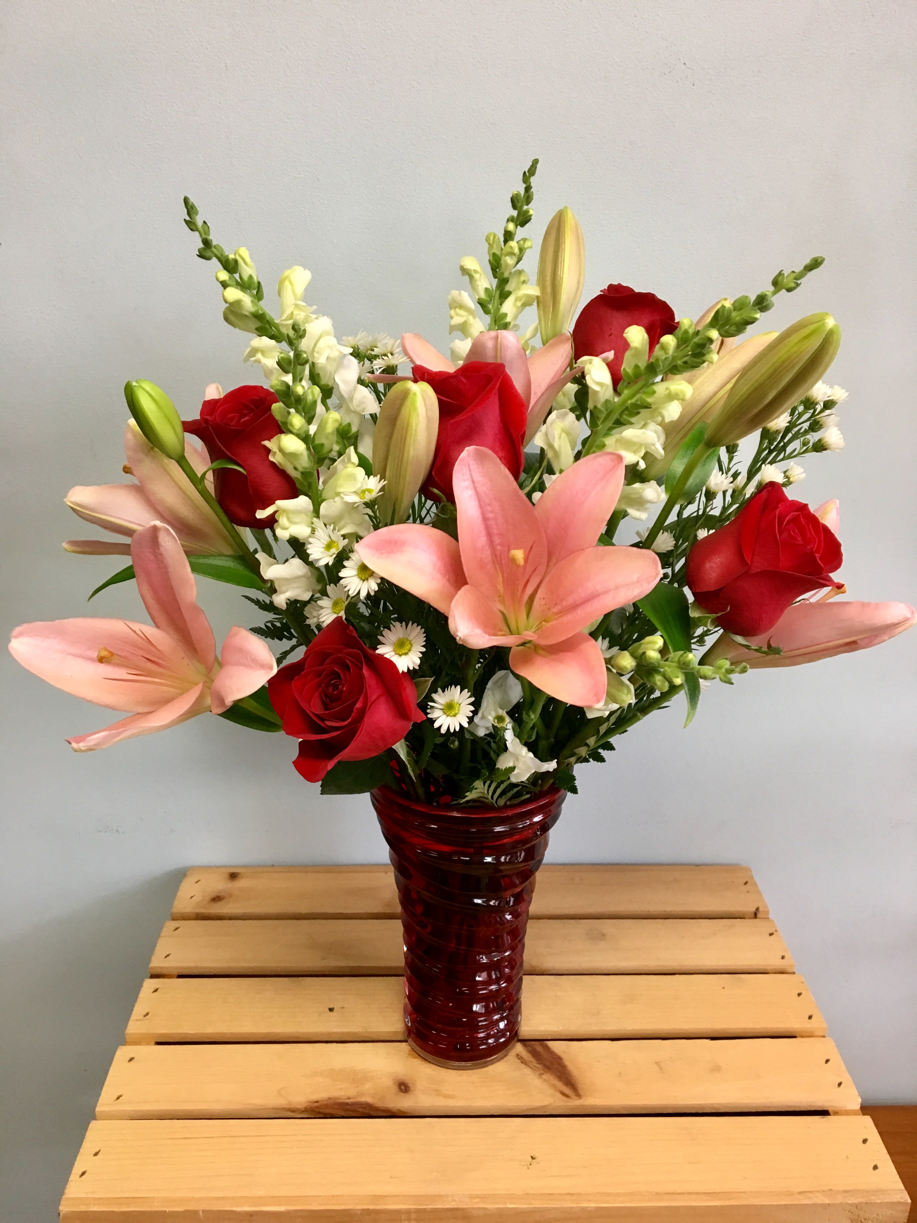 Bouquet of pink lilies and red roses in a red glass vase
