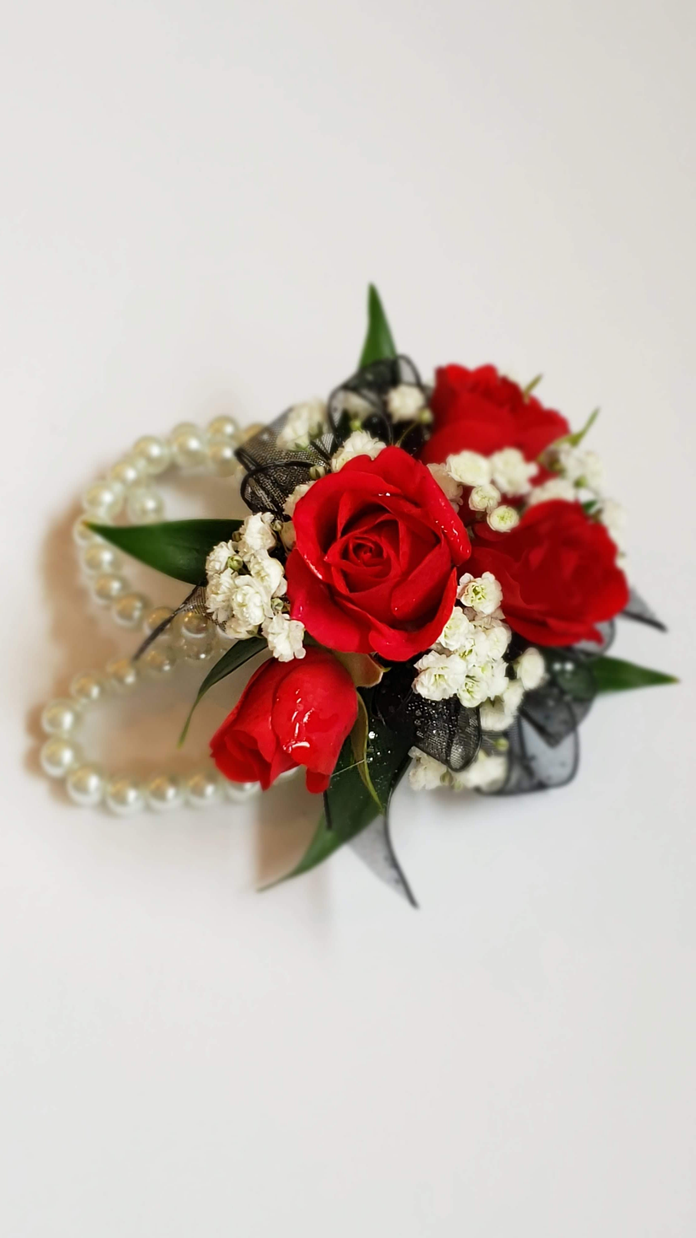 Red rose corsage with white filler flowers and pearl bracelet