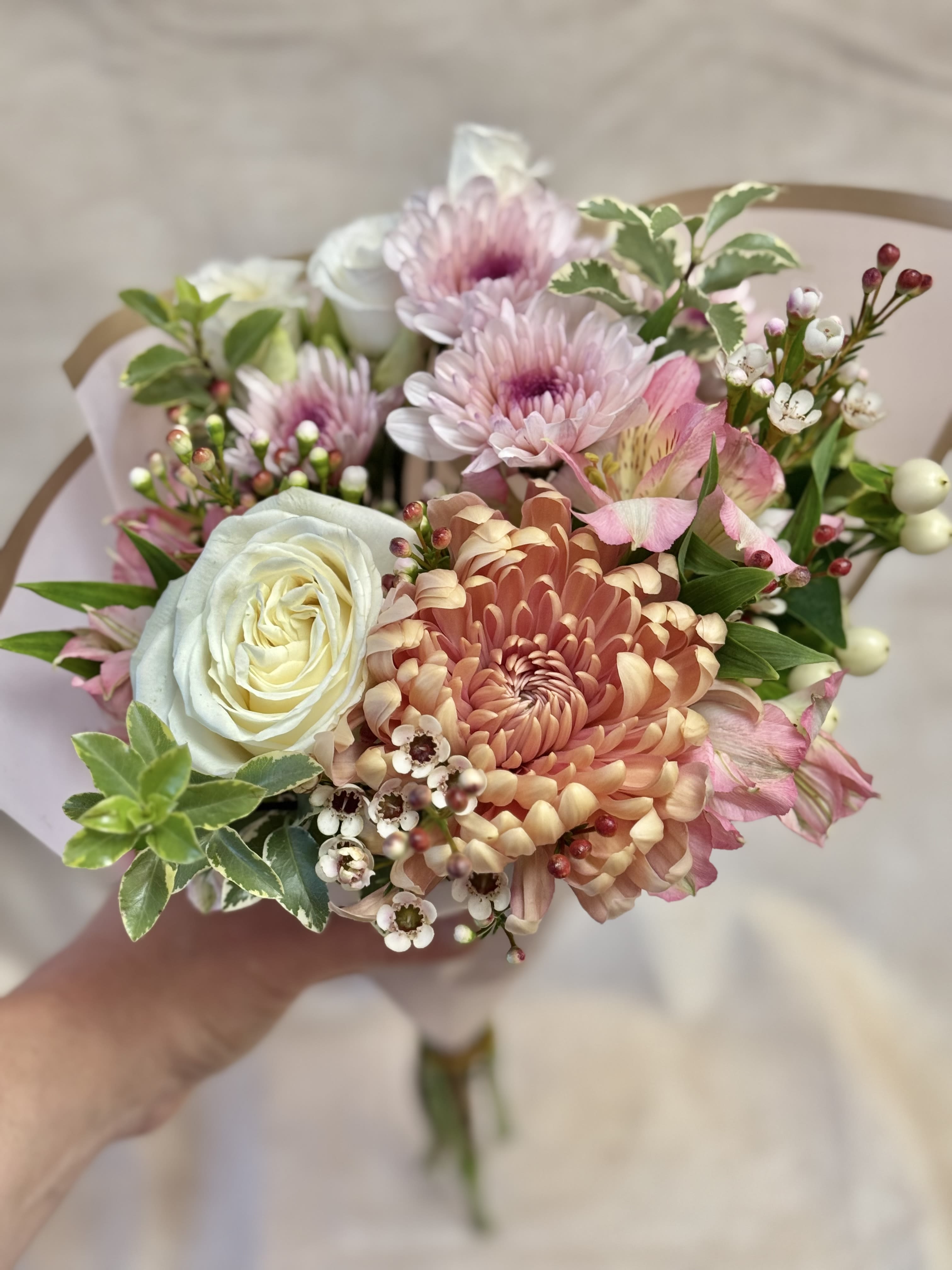 Handheld bouquet of pink and white flowers with a peach chrysanthemum