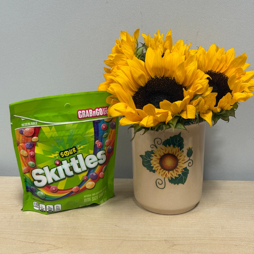 Sunflowers in a ceramic vase beside a bag of Sour Skittles candy