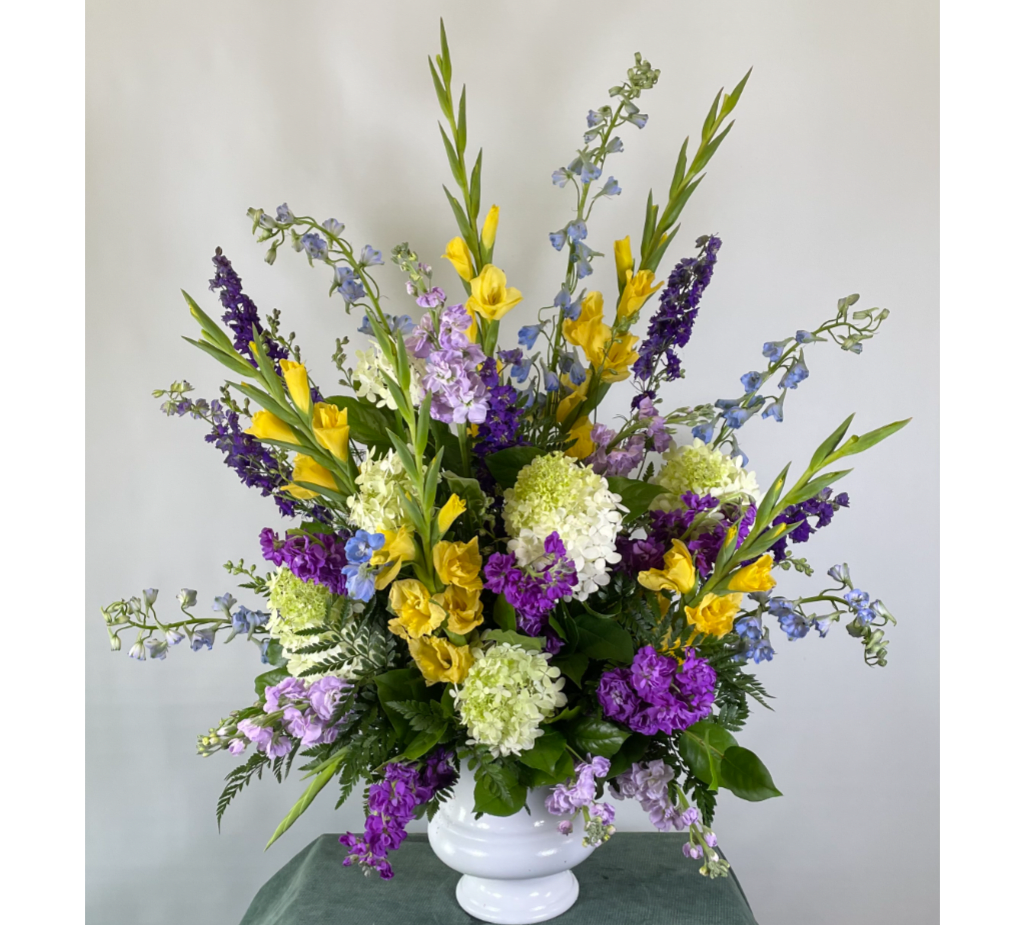 Tall mixed bouquet in a white vase with yellow, purple, blue, and white flowers