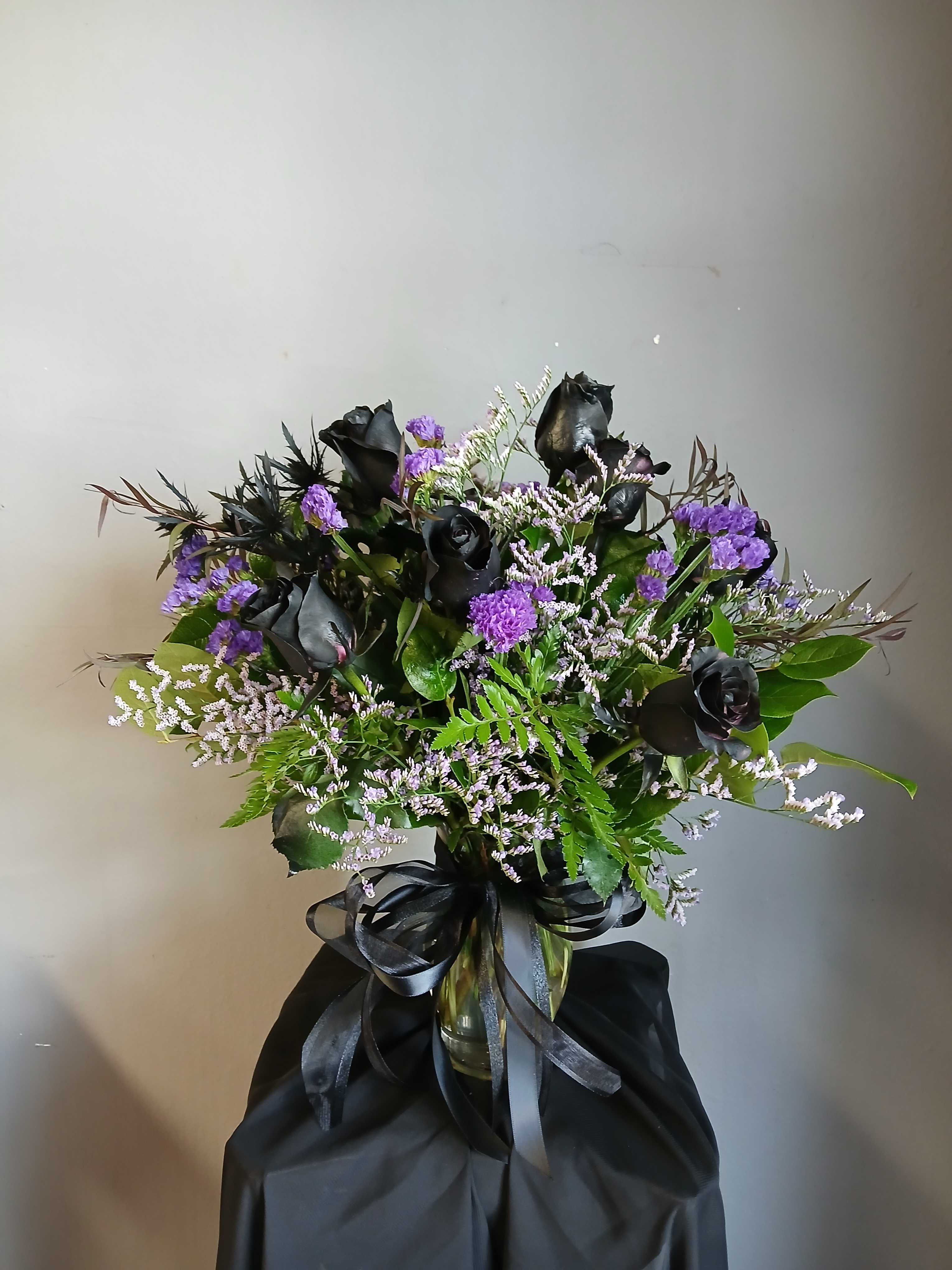 Black roses and purple filler flowers in a glass vase with a black ribbon
