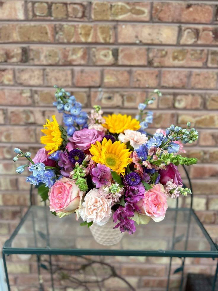 Mixed bouquet of pink, purple, blue, and yellow flowers in a white vase