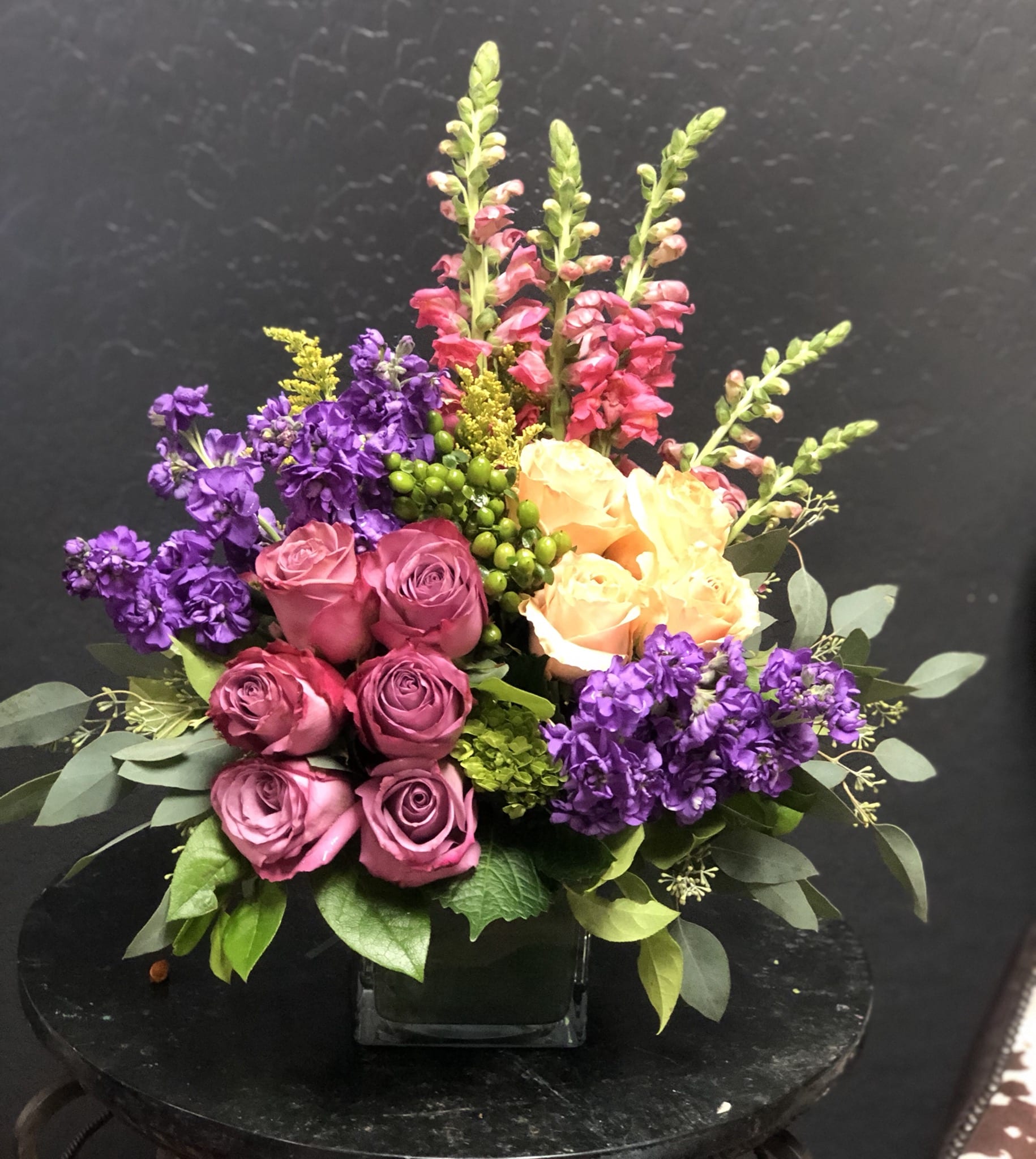Bouquet of pink and peach roses with purple flowers in a glass vase