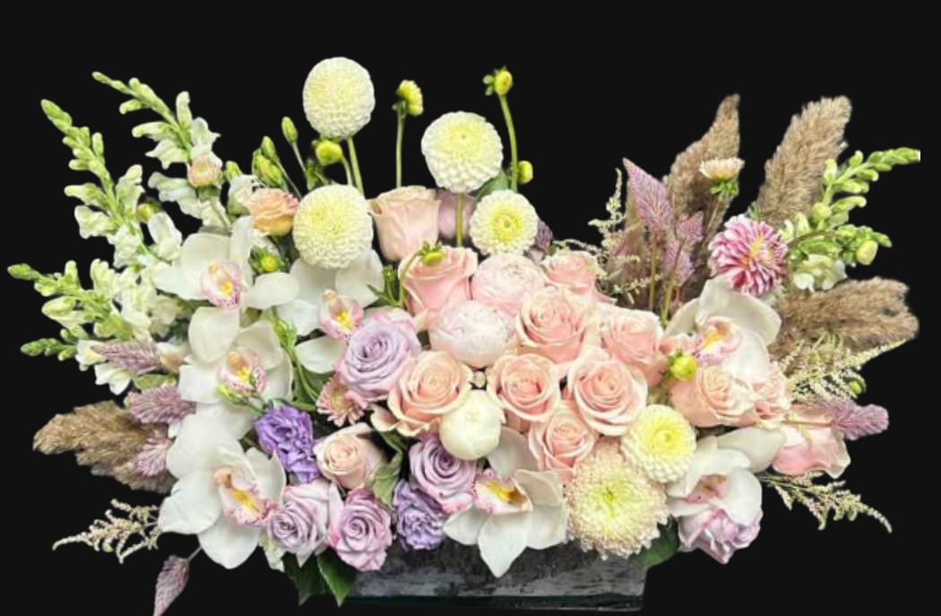 Pastel floral arrangement with roses, orchids, and round white blooms in a low container