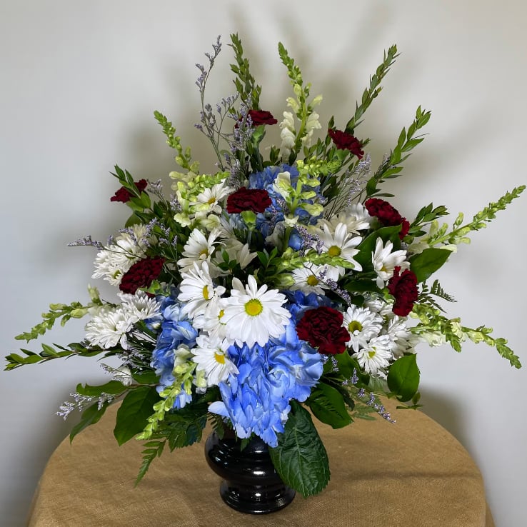 Mixed bouquet in a black vase with white daisies, blue hydrangeas, and red carnations